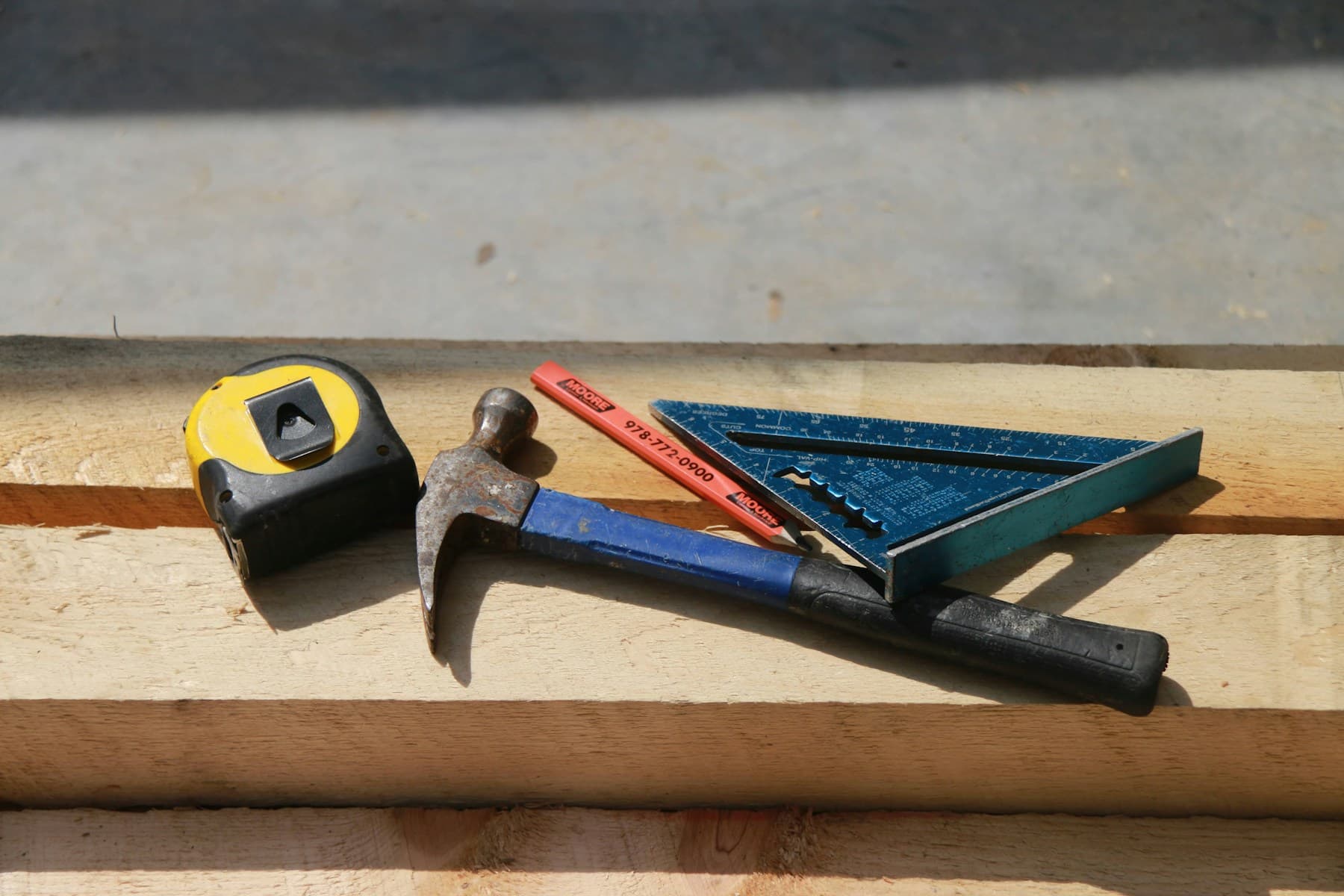 Worn hammer, tape measure and square on timber